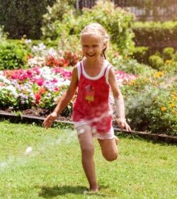 child running through sprinkler in yard